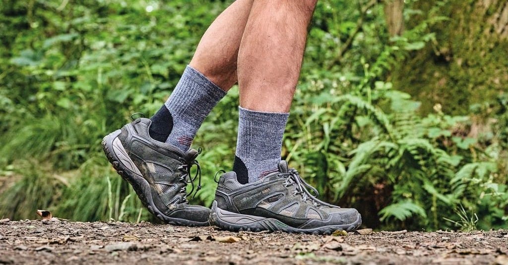 A hiker in boots and socks against a background of greenery 