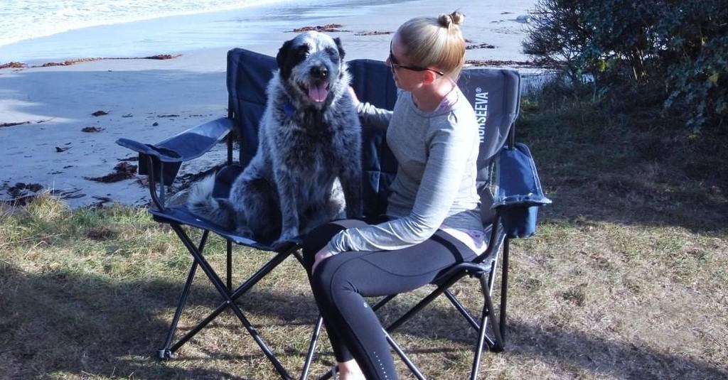 Girl sitting with dog behind two camping chairs