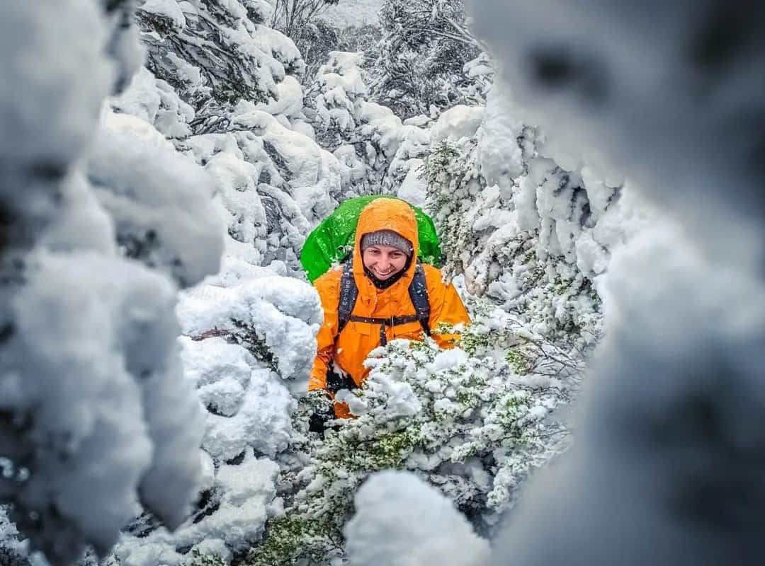A hiker in an orange jacket in a snowy forest