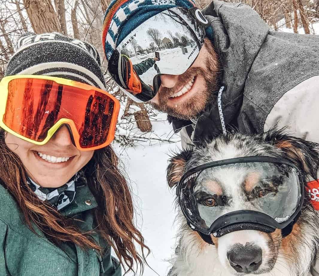 man woman and dog in ski goggles